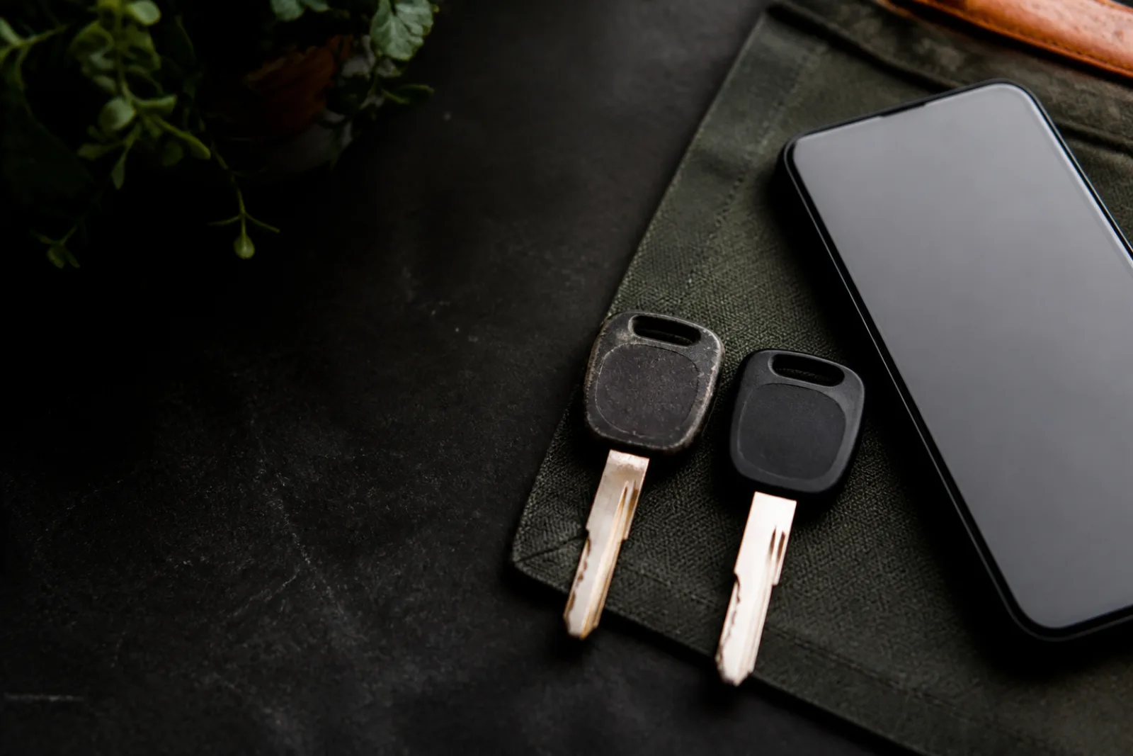 Worn and clean automotive keys compared beside a phone with a blank screen.